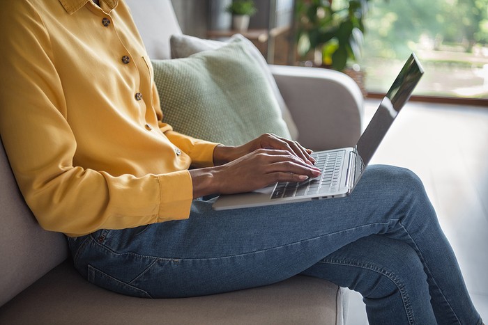 Woman Sitting on Sofa Typing on Laptop